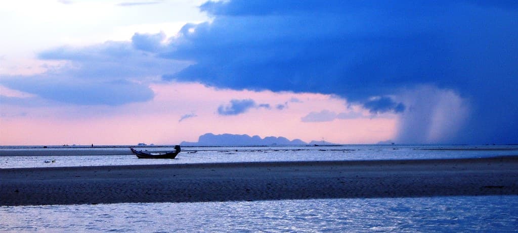Koh Phangan shoreline at dusk with a long-tail boat and storm light