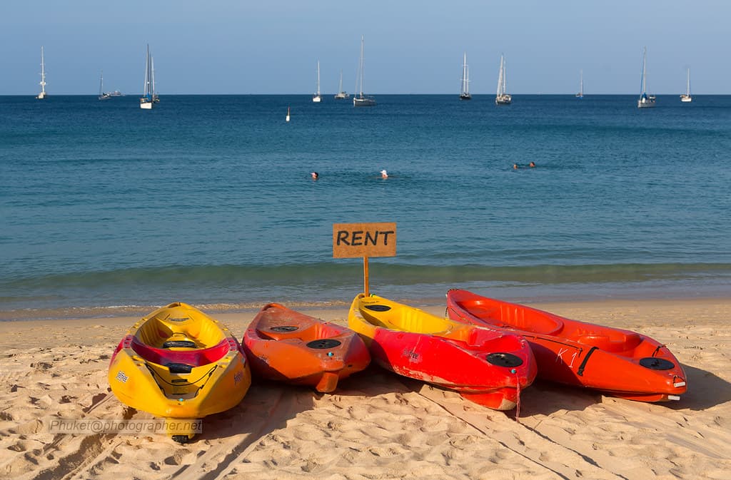 Bright kayaks resting on a Thailand beach near clear water