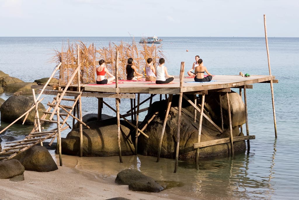 Small group practicing yoga beside calm Thailand water